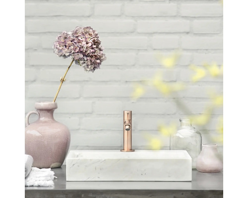 Badezimmerwaschtisch mit Armatur, Blumenvase und dekorativen Elementen vor einer weißen Ziegelwand