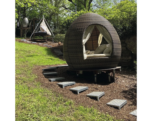 Scène de jardin avec un lit d''extérieur rond et couvert et un hamac sur une colline verdoyante