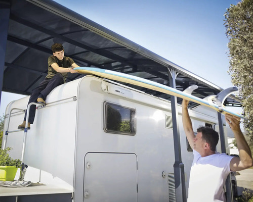Personen laden Surfbrett auf ein Wohnmobil unter einem Carport