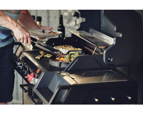 Un homme fait griller des légumes sur un barbecue à gaz.