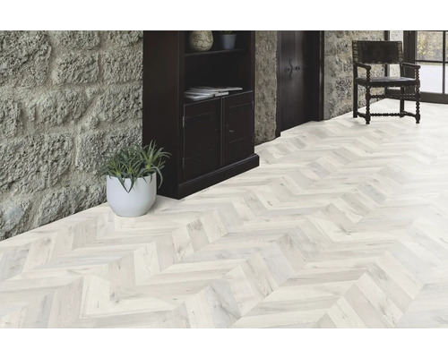 Pièce lumineuse avec parquet à chevrons, escalier en pierre et armoire en bois foncé.