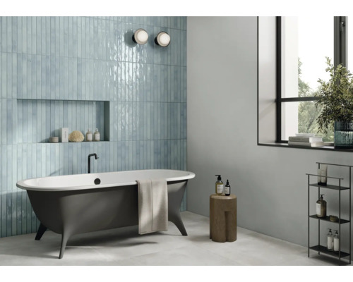 Badezimmer mit blauen Fliesen, freistehender Badewanne und Fenster für eine helle, freundliche Atmosphäre.