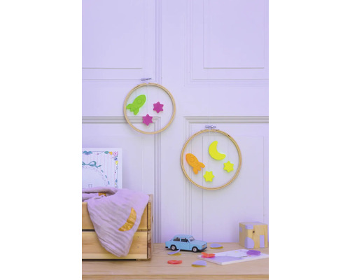 Scène décorative de chambre d''enfant avec des cerceaux à broder, des fusées, des étoiles, un croissant de lune, une voiture jouet et une caisse en bois sur une table devant un mur