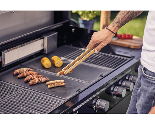 Un homme fait griller des saucisses et des épis de maïs sur un gril