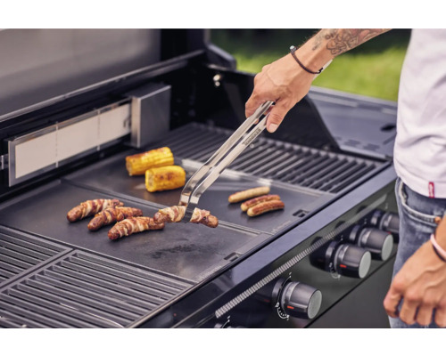 Person grilliert Würstchen, Speck und Maiskolben auf einem Grill.