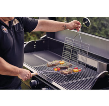 Person grilliert Steaks und Gemüse mit einem Grillkorb auf einem Gasgrill.