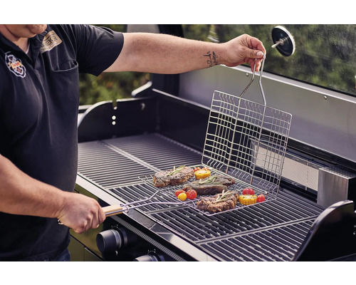 Person grilliert Steaks und Gemüse mit einem Grillkorb auf einem Gasgrill.