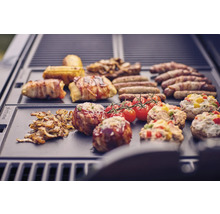 Verschiedene Speisen wie Würstchen, Speck, Tomaten und gefüllte Champignons auf einem Grill.