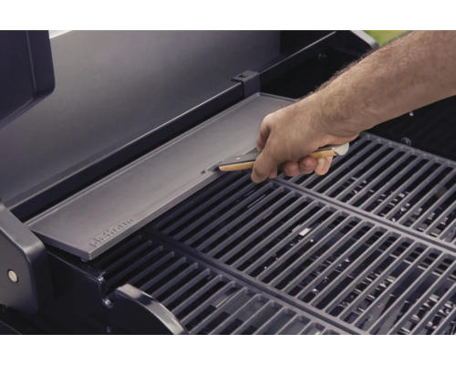 Un homme place une plaque de gril sur une grille de barbecue.
