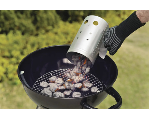 Une personne verse du charbon de bois d''une cheminée d''allumage dans un barbecue boule.