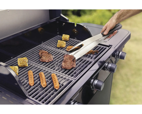 Barbecue avec des aliments grillés tels que des steaks, des saucisses et des épis de maïs, manipulés avec une pince.