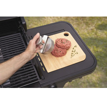 Une personne forme des galettes de hamburger à l''aide d''une presse à hamburger sur une planche à découper à côté d''un barbecue.