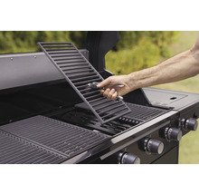 Une personne place une grille de barbecue dans un barbecue à gaz.