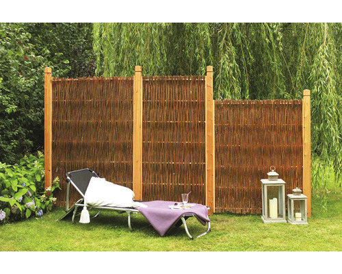 Scène de jardin avec brise-vue en osier et poteaux en bois, chaise longue et lanternes