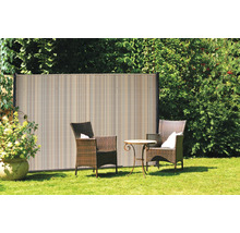 Scène de jardin avec écran d''intimité en plastique, fauteuils en rotin et petite table sur une pelouse.