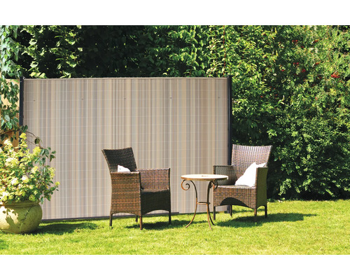 Scène de jardin avec écran d''intimité en plastique, fauteuils en rotin et petite table sur une pelouse.