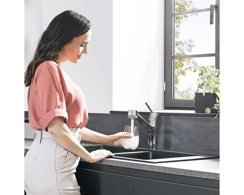 Frau füllt Wasser in ein Glas am Spültisch mit Wasserhahn in der Küche.