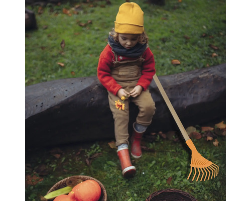 Fille assise à côté du râteau dans le jardin