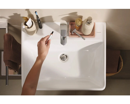 Vue de dessus d''un lavabo de salle de bains avec robinetterie et divers accessoires de salle de bains, une main tenant un coupe-poils de nez.
