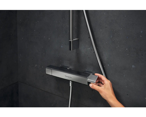 Aufnahme einer Hand, die einen Duschthermostat von Hansgrohe in einem Badezimmer bedient