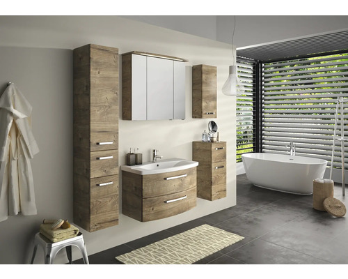 Salle de bains avec lavabo, armoire de toilette et armoire haute à l''aspect bois, ainsi que baignoire et porte-serviettes.