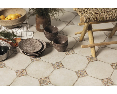 Les carreaux de sol décoratifs avec des accents floraux, combinés à de la vaisselle, des bols et un tabouret en bois, créent une atmosphère de cuisine chaleureuse.