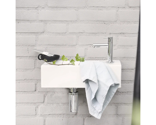 Salle de bain moderne avec lavabo blanc, robinetterie chromée et serviette devant un mur de briques