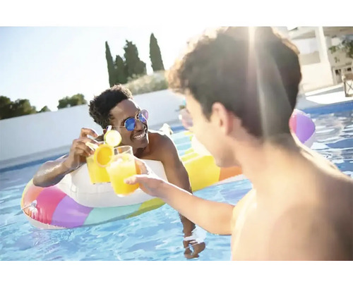 Deux hommes trinquent avec des boissons dans une piscine avec une bouée gonflable.
