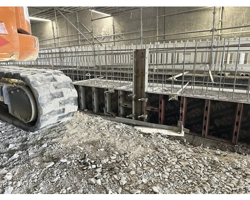 Baugrube mit Schalung und Armierungseisen, Raupenbagger im Vordergrund.