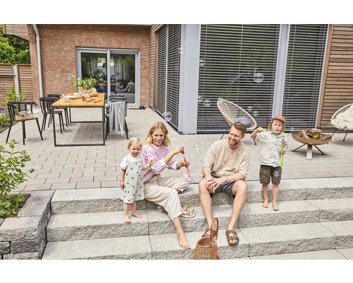 Une famille joue avec des bulles de savon sur une terrasse avec des dalles en pierre et un escalier
