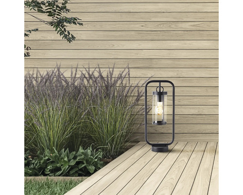 Dekorative Aussenleuchte aus Metall und Glas auf einer Holzterrasse neben einer Pflanzenreihe.