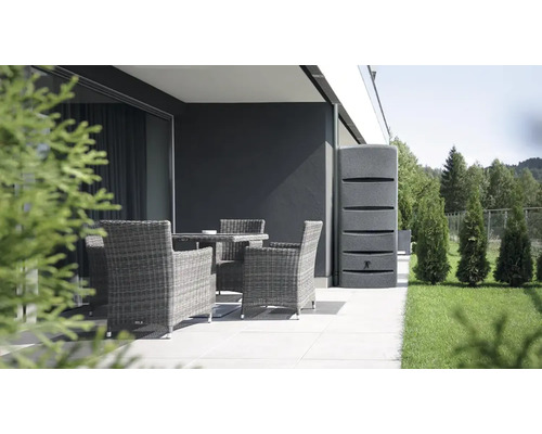 Gartenszene mit grauer Regentonne neben einer Terrasse mit Rattansesseln und Tisch