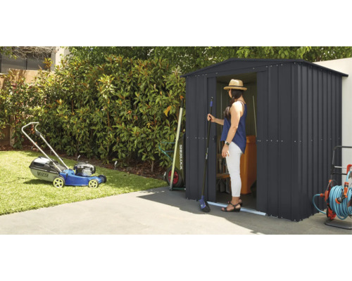 Scène de jardin avec tondeuse à gazon et cabanon dans lequel se tient une femme