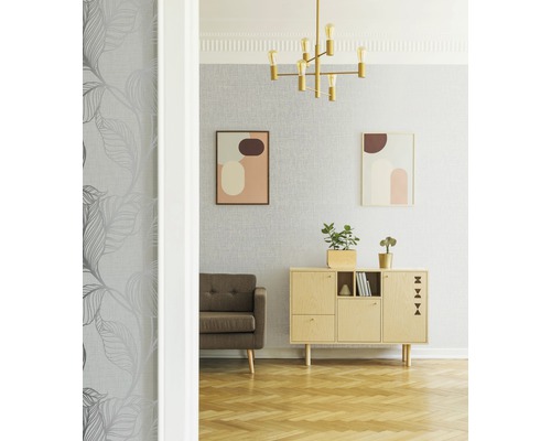 Salon avec papier peint à feuilles grises, canapé marron, commode et lampe dorée