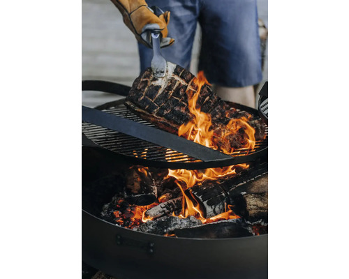 Grillgut wird über einem Holzkohlegrill mit einer Zange gewendet