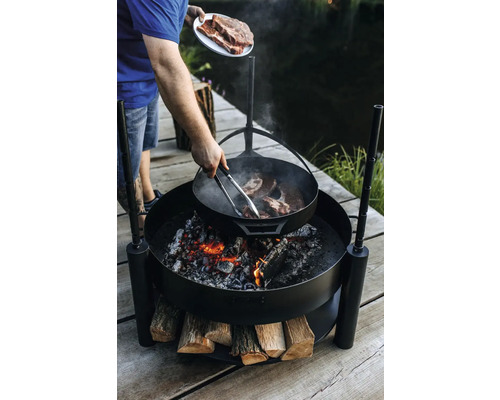 Personne préparant des steaks sur un foyer extérieur.