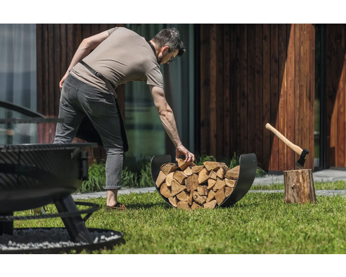 Un homme remplit un support à bûches avec des bûches à côté d''un billot avec une hache dans le jardin.