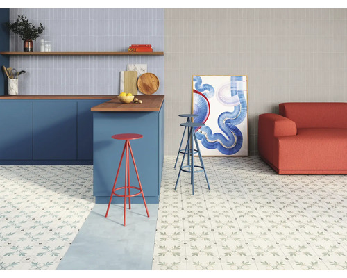 Cuisine et salon lumineux avec carrelage à motifs floraux, comptoir avec tabourets de bar et canapé.