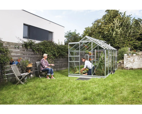 Gewächshaus im Garten mit zwei Frauen, eine gärtnernd, die andere sitzend.