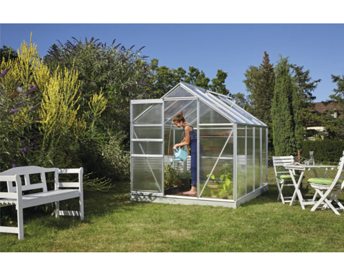 Serre dans le jardin avec une femme arrosant les plantes