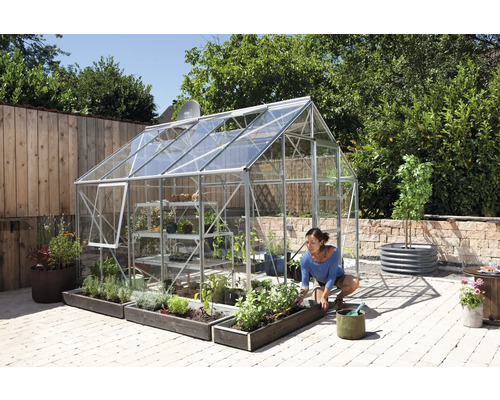 Gewächshaus mit Pflanzen und einer Frau, die im Garten arbeitet.