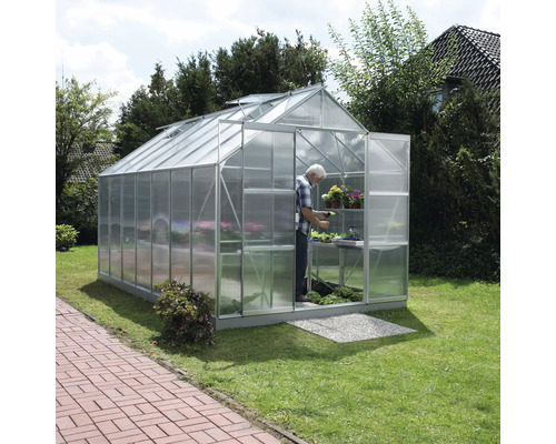 Serre avec personne, plantes et étagères dans le jardin.