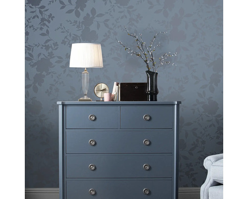 Kommode mit Lampe, Uhr und Dekoration vor floral gemusterter Wand