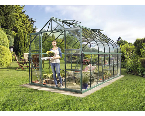 Gewächshaus im Garten mit einer Frau, die eine Pflanze trägt.