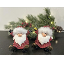 Deux figurines décoratives de Père Noël sont assises devant une guirlande de sapin enneigée.