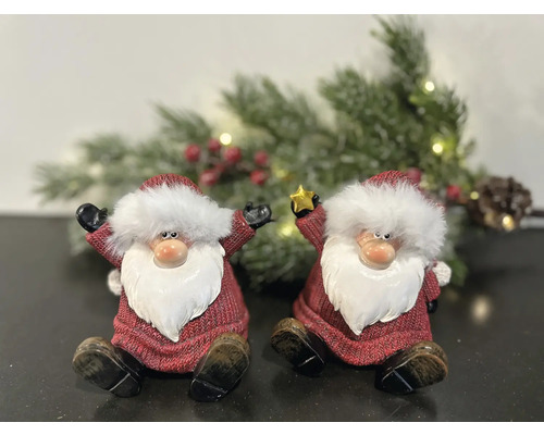 Deux figurines décoratives de Père Noël sont assises devant une guirlande de sapin enneigée.