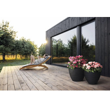 "Scène avec une femme se relaxant sur une chaise longue en bois sur une terrasse en bois devant une maison avec de grandes fenêtres 