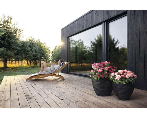 "Scène avec une femme se relaxant sur une chaise longue en bois sur une terrasse en bois devant une maison avec de grandes fenêtres 