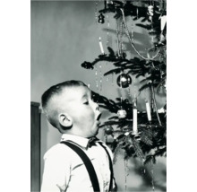 Ein Junge betrachtet mit offenem Mund einen Weihnachtsbaum mit Schmuck, Kerzen und Kugeln.