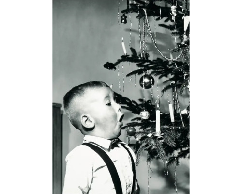 Ein Junge betrachtet mit offenem Mund einen Weihnachtsbaum mit Schmuck, Kerzen und Kugeln.